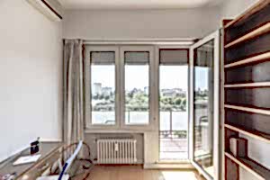 Large window of a room with an exit door to a terrace with views of an urban park