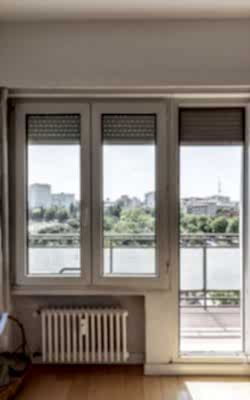 Large window of a room with an exit door to a terrace with views of an urban park
